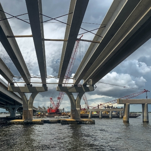 Bridge construction project with cranes operating between concrete spans over a Florida waterway