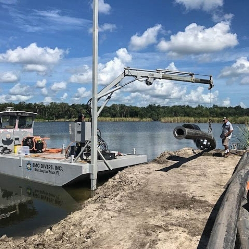 EMC Divers barge with crane installing a concrete pipe along a Florida shoreline