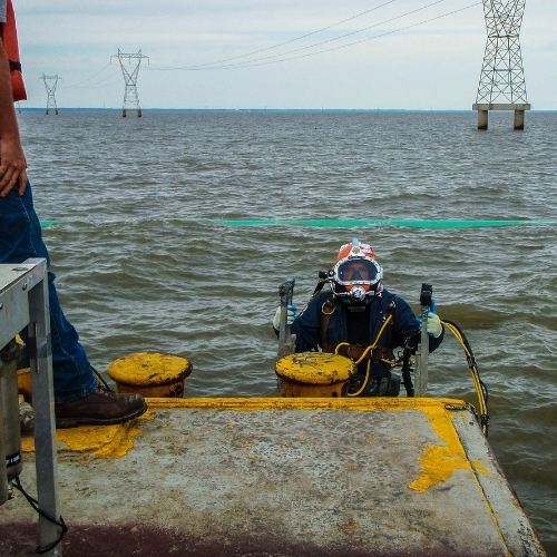 Commercial diver inspecting waterfront infrastructure with surface access