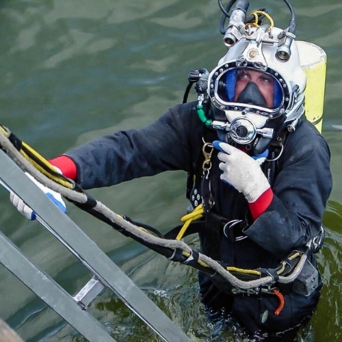 Commercial diver descending a ladder for water access with surface equipment