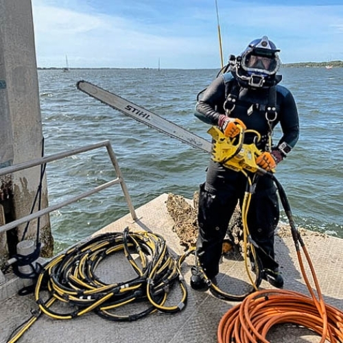 Commercial diver staged with hydraulic chainsaw for underwater cutting work