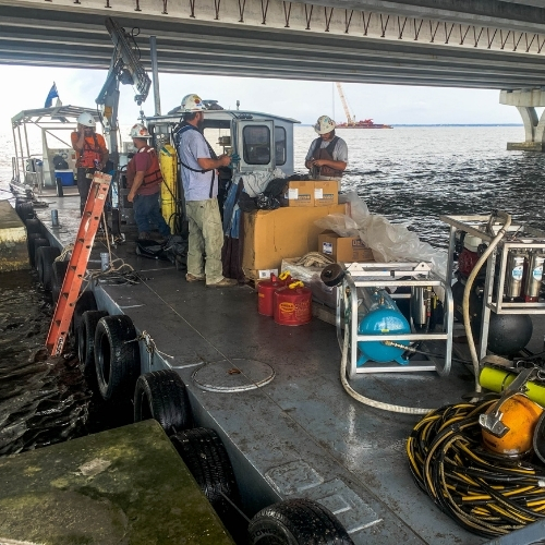 Commercial diving crew staged on a barge beside a bridge project with surface-supply equipment