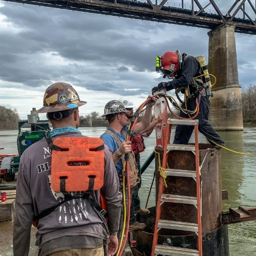 Commercial diving crew supporting a bridge inspection from a ladder