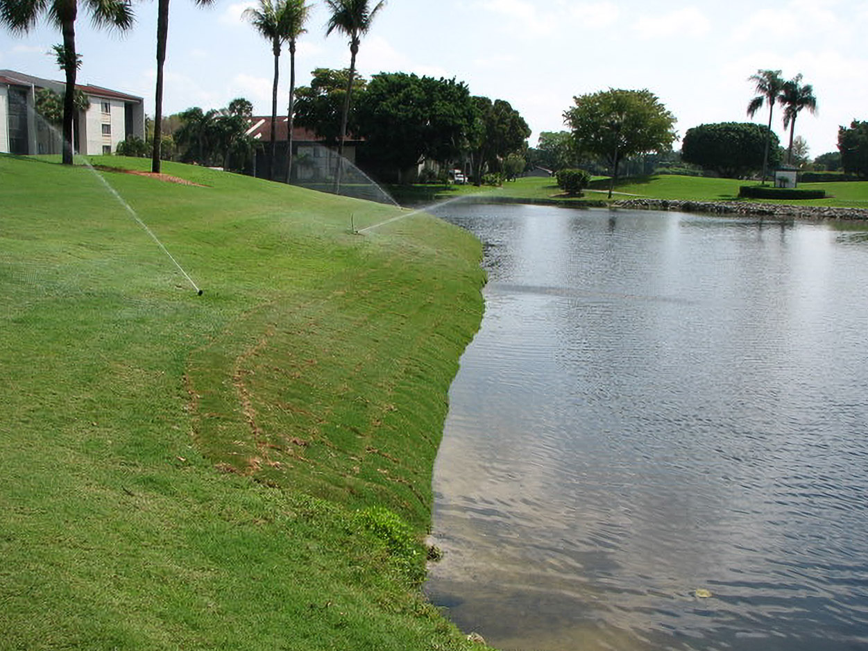 Sprinklers watering freshly sodded bank along a Yacht, Golf & Tennis pond after restoration