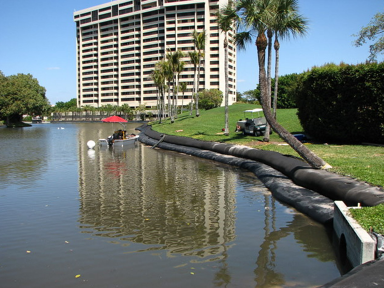 Geo Tube along a Yacht, Golf & Tennis pond bank with golf cart and high-rise beyond