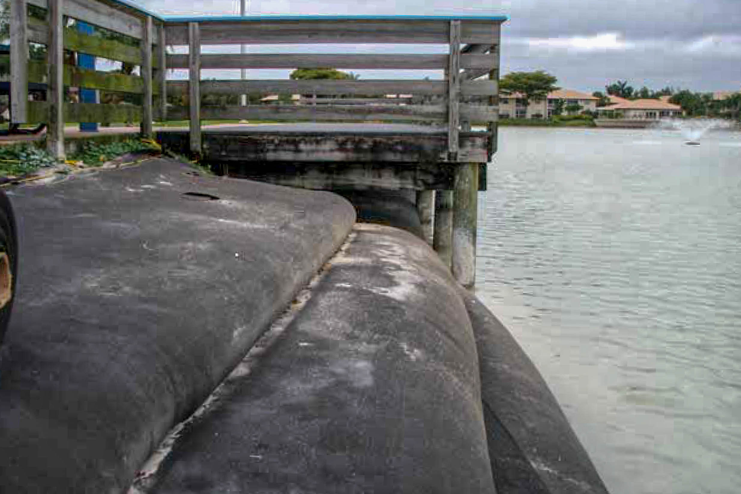 Wooden pier and stacked Geo Tubes along a municipal pond with a fountain in the distance
