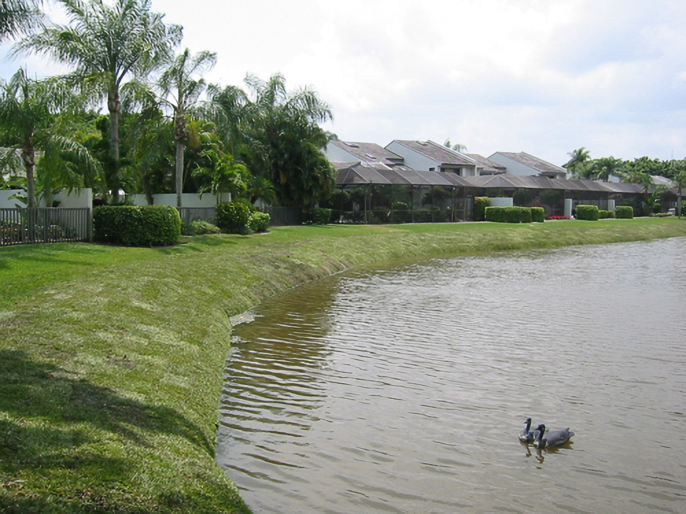 Restored grassy shoreline curving past Boca West townhomes after lake bank stabilization
