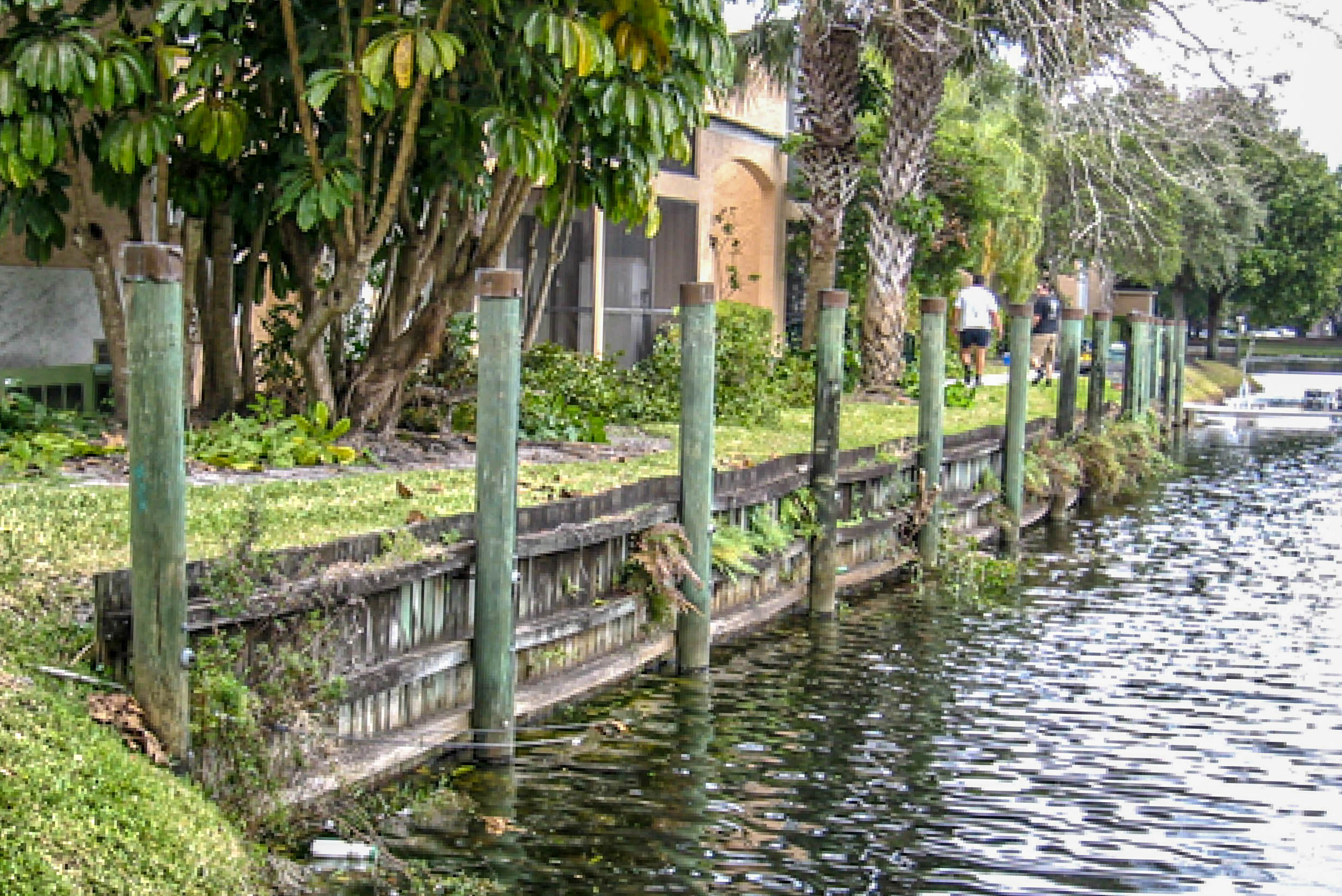 Green fence posts along an eroded AIMCO community canal before restoration