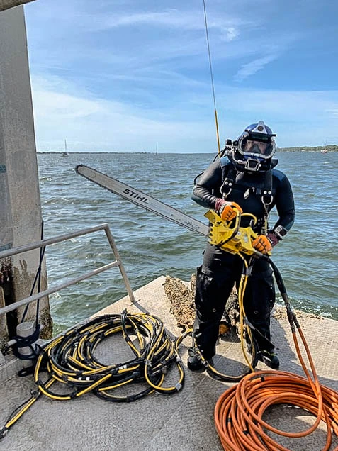 Commercial diver staged with hydraulic chainsaw and air supply for underwater cutting work