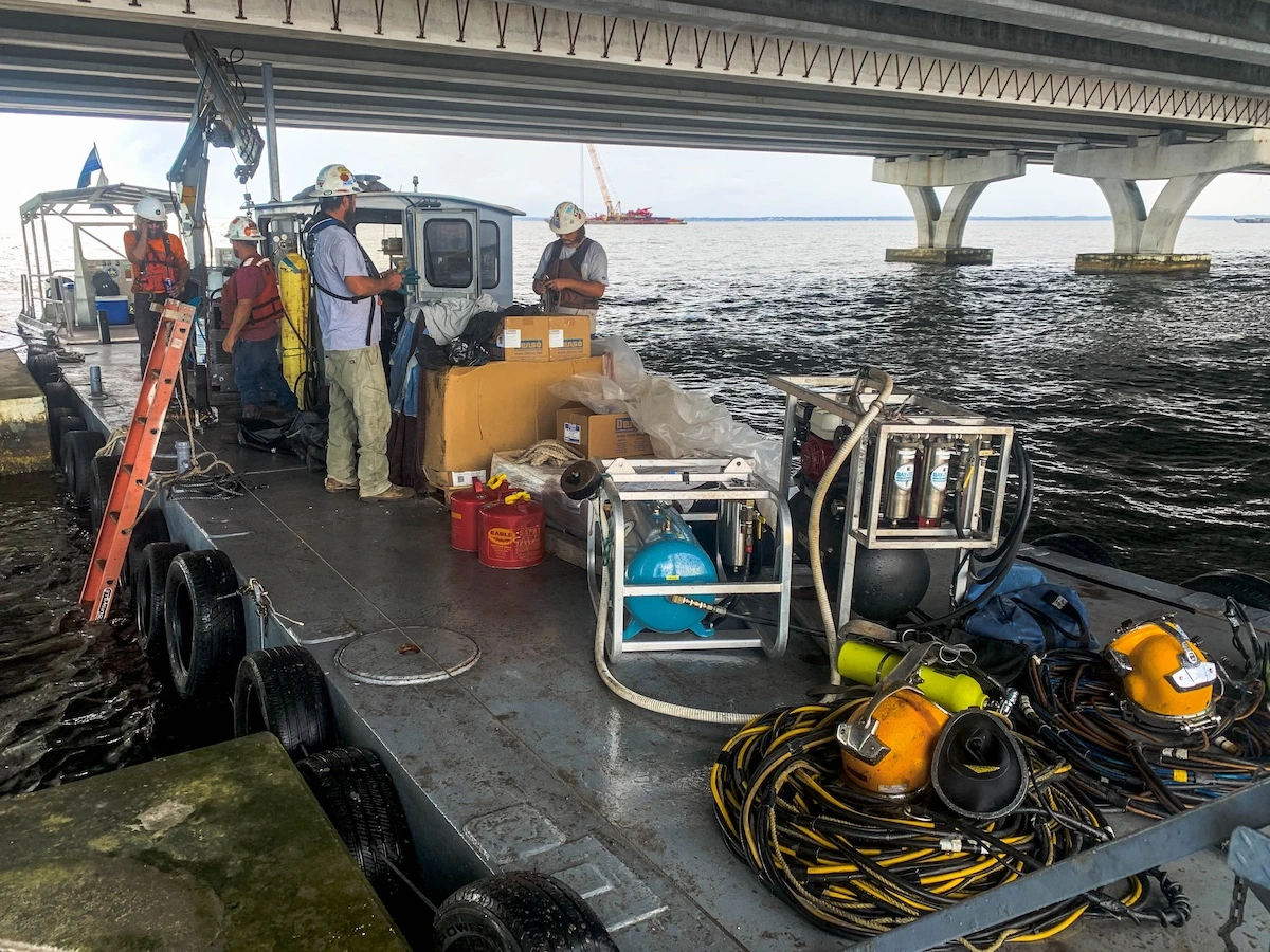 Commercial diving crew staged on a barge with surface-supply equipment beside a Florida bridge project