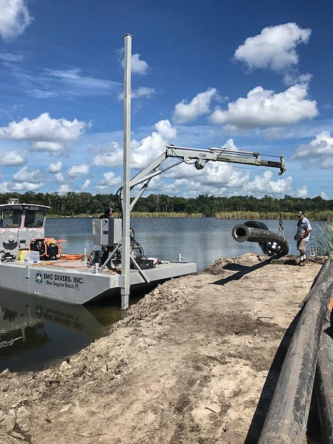 EMC Divers barge with mounted crane installing a concrete pipe along a Florida shoreline